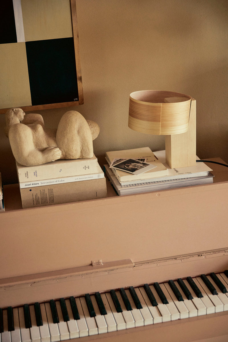 Piano with books, a lamp, and a sculpture on top in a warm-toned room.